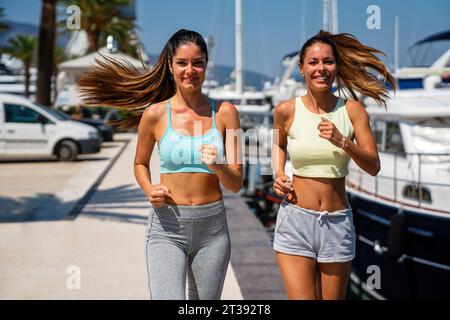 Zwei glückliche Frauen, die bei Sonnenaufgang laufen. Fröhliche, multiethnische Jogger im Freien Stockfoto