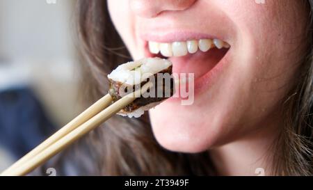 Eine junge Frau, die eine Sonnenbrille trägt und Essstäbchen hält, genießt eine Mahlzeit Sushi Stockfoto
