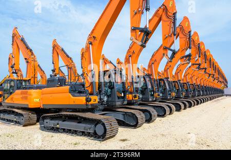 Dutzende brandneuer orangefarbener caterpillar-Hydraulikbagger reihten im Freien unter stürmischem Himmel in einer Reihe an. Stockfoto