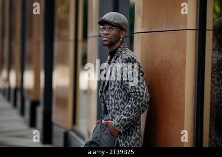 Porträt afroamerikanischer junger Mann im trendigen Outfit Mantel mit Tierdruck, Rollkragen, Baskenmütze, Hose und Brille, auf der Stadtstraße. Hand Stockfoto
