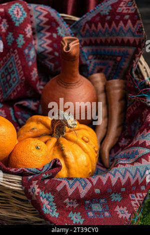 Eine rustikale Ausstellung mit einem Tontopf, leuchtenden Orangen, einem Kürbis und traditionellen gewebten Stoffen mit komplizierten Mustern in Rot- und Blautönen Stockfoto