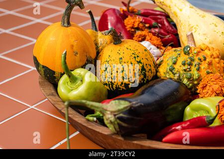 Kürbisse, Auberginen und Paprika in einer großen Holzschale auf einem Terrakottaböden. Stockfoto