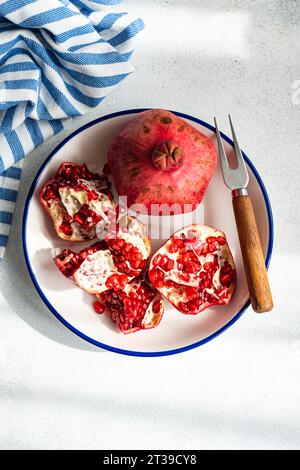 Ansicht von oben auf reifem Granatapfel offen auf blauem Rand Platte mit einem rustikalen Holzgriff Messer auf einem grauen Texturhintergrund. Stockfoto