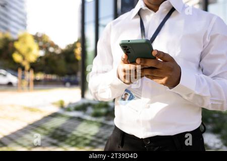 Anonymes Porträt eines afroamerikanischen männlichen Unternehmers in formeller Nachricht per Smartphone senden, während er auf der Straße steht und auf den Bildschirm blickt Stockfoto