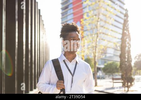 Durch Glasreflexion Porträt eines jungen afroamerikanischen Mannes in weißem Hemd, der wegschaut, während er in der Nähe eines modernen Gebäudes an der Stadtstraße steht Stockfoto