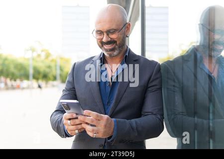 Porträt eines bärtigen und kahlen Geschäftsmannes, der sein Smartphone auf der Straße benutzt Stockfoto