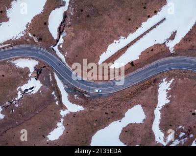 Aus der Vogelperspektive auf eine kurvige Straße, umgeben von Schneebesen, mit einem Fahrzeug, das entlang der Straße in Cerler, Huesca, Spanien fährt Stockfoto