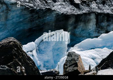 Nahaufnahme eines Gletschers mit eisigen Formationen inmitten von Felsen unter Sonnenlicht. Stockfoto