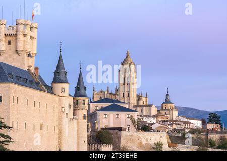 Blick aus der Vogelperspektive auf das alte Schloss Alcazar von Segovia Spanien, das sich auf einem Hügel mit Bäumen vor dem bewölkten Sonnenuntergangshimmel in der Dämmerung befindet Stockfoto