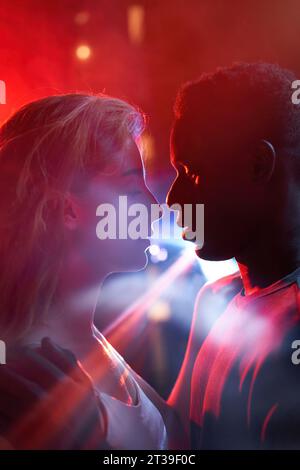 Porträt von jungen Menschen, die sich in Nahaufnahme betrachten, umgeben von leuchtenden roten Lichtern, die tiefe Emotionen und Verbindung vermitteln Stockfoto