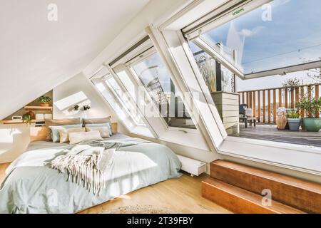 Sonnenlicht fällt durch große Fenster im Schlafzimmer im Dachgeschoss des modernen Hauses auf das komfortable Bett Stockfoto