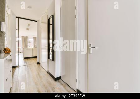 Schmaler Flur mit Türen zu verschiedenen Zimmern und Spiegel an weißer Wand in einem modernen Apartment Stockfoto