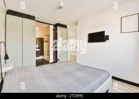 Komfortables Bett mit Fernseher und Kleiderschrank im geräumigen weißen Schlafzimmer des modernen Apartments Stockfoto
