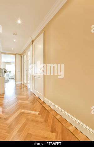 Leerer langer Flur mit beigefarbenen Wänden und weißen Türen führt zu verschiedenen Zimmern in einem modernen Apartment Stockfoto
