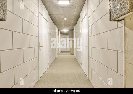 Langer schmaler Korridor mit weißen Fliesentüren mit geschlossenen Türen von Lagerräumen in Industriegebäuden zur Vermietung Stockfoto