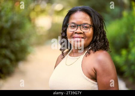 Porträt einer afroamerikanischen Frau mit lockigen Haaren, die im Garten lächelt. Stockfoto