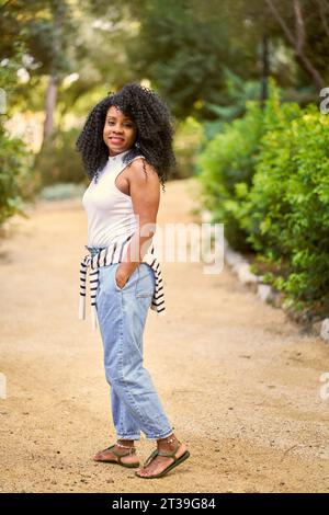 Porträt einer afroamerikanischen Frau mit lockigen Haaren, die im Garten lächelt. Stockfoto