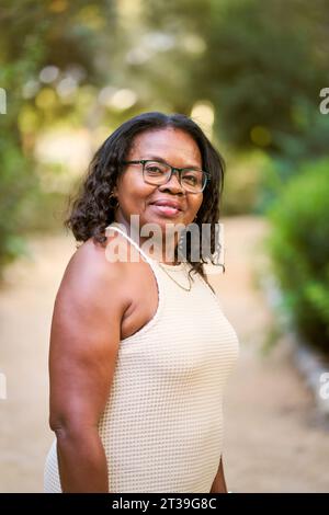 Porträt einer afroamerikanischen Frau mit lockigen Haaren, die im Garten lächelt. Stockfoto