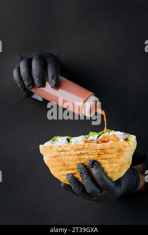 Kocht mit der Hand Soße in Döner-Döner durch gerissene Löcher auf schwarzem Papierhintergrund. Street Food Stockfoto