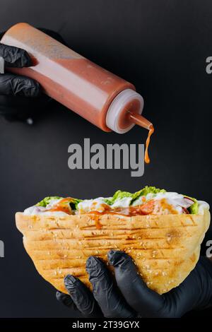 Kocht mit der Hand Soße in leckeren Döner-Döner-Kebab durch gerissene Löcher auf schwarzem Papierhintergrund Stockfoto