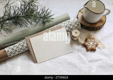 Weihnachtsstillleben. Grußkarte, Einladungsmockup. Lebkuchenkekse, Tannenzweige auf weißem Leinentischtuch. Geschenkpapier mit Stockfoto