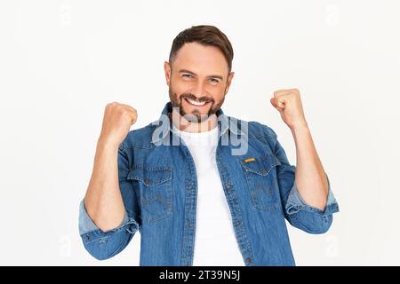 Porträt eines jungen gutaussehenden Mannes mit Bart, der legere Kleidung auf weißem Hintergrund trägt. Sehr glücklich und aufgeregt, die Siegergeste mit erhobenen Armen zu tun, sm Stockfoto
