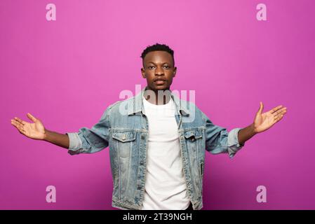 Junger afrikanischer Mann, der in die Kamera schaut mit Hand geöffneter Geste in violettem Farb-Studio isoliertem Hintergrund Stockfoto