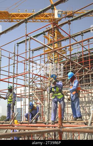 Ausländische Arbeiter aus Indien und Pakistan bauen Gerüste auf einer großen Baustelle in Abu Dhabi, VAE. Stockfoto