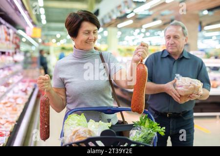 Reifes Paar, das sich im Supermarkt fleißig leckere Würstchen aussucht Stockfoto