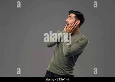 Schockierter kaukasischer Mann, der seitlich mit Händen auf den Wangen schaut, in hellgrauem, isoliertem Hintergrundfoto Stockfoto