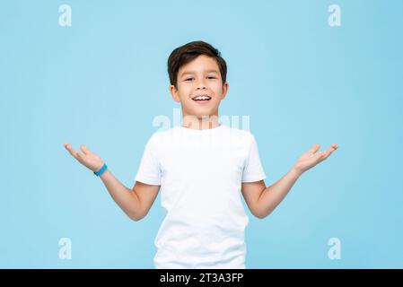 Niedlicher gemischter Rassenjunge lächelt und öffnet Hände, die Willkommensgeste in hellblauer Farbe tun isolierte Hintergrundaufnahme im Studio Stockfoto