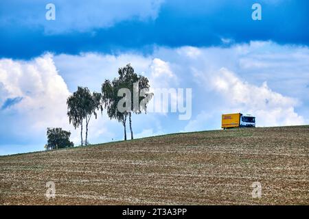 DHL Delivery Truck fährt auf rollenden Hügeln unter hellem blauen Himmel mit Wolken in Frankreich. Stockfoto