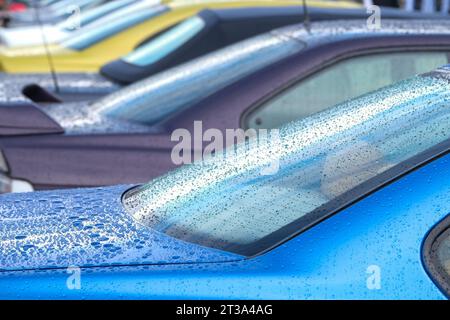 Nahaufnahme von Wassertropfen auf den bunten blauen lila Autos. Wasserperlen nach Regen oder Autowäsche auf der Oberfläche. Regnerisches Wetter und Fahrzeugkonzept. Stockfoto