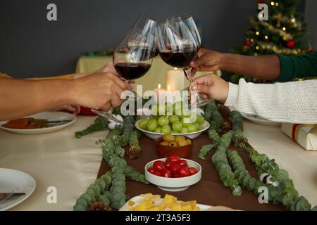 Freunde, die zu Hause mit Weingläsern über dem Weihnachtstisch tosten, wenn sie zu Hause feiern Stockfoto