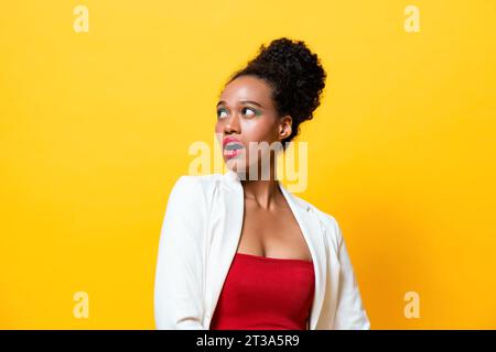 Modische afroamerikanische Frau mit farbenfrohem Make-up, das schockiertes Gefühl ausdrückt, seitlich in isolierter gelber Hintergrundaufnahme im Studio schaut Stockfoto