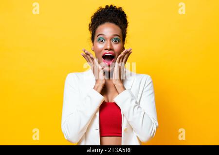 Modische afroamerikanische Frau mit farbenfrohem Make-up, die ein schockiertes aufgeregtes Gefühl mit Händen auf den Wangen in isoliertem gelbem Hintergrund ausdrückt Stockfoto