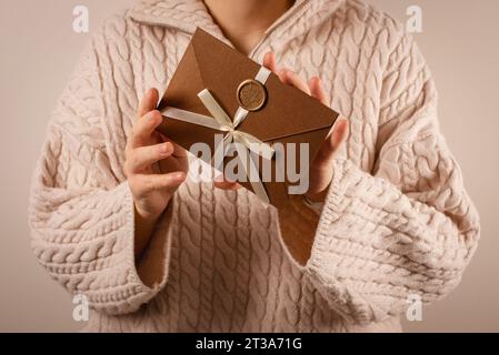 Frau in kuscheliger Strickpullover mit Geschenkkarte oder Einladung zu handgemachter Meisterklasse oder Lehre Stockfoto