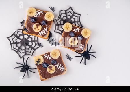 Lustige Halloween Bär Toast Sandwiches mit Nüssen, Schokoladenbutter, Paste, Banane und geschmolzenem Marshmallow oder Joghurtnarben Dekor. Kreatives Halloween-Mittagessen Stockfoto