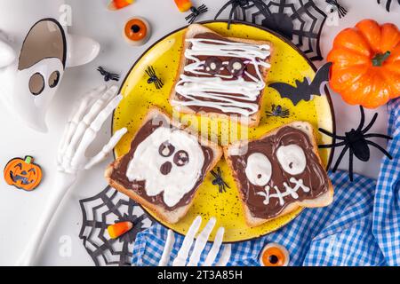 Lustige Halloween-Charaktere toasten Sandwiches mit Nüssen, Schokoladenbutter, Paste, Banane und geschmolzenem Marshmallow oder Joghurtnarben Dekor. Kreatives Halloween Stockfoto