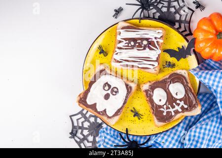 Lustige Halloween-Charaktere toasten Sandwiches mit Nüssen, Schokoladenbutter, Paste, Banane und geschmolzenem Marshmallow oder Joghurtnarben Dekor. Kreatives Halloween Stockfoto