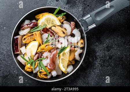 Roher Mix Meeresfrüchte-Cocktail mit Garnelen, Garnelen, Muscheln, Tintenfischen und Tintenfischen in einer Pfanne bereit zum Kochen. Schwarzer Hintergrund. Draufsicht. Stockfoto