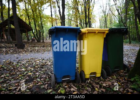 Drei gelbe, blaue und grüne Recyclingbehälter im Herbstpark am Boden. Stockfoto