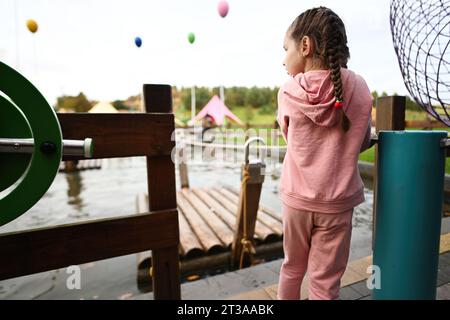 Entzückendes kleines Mädchen, das sich auf dem Spielplatz im Freien amüsiert. Niedliches Kind, das draußen spielt. Stockfoto