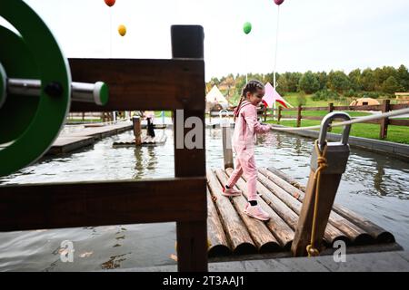 Kleines Mädchen im rosa Jumpsuit, das auf dem Pier im See spielt. Stockfoto