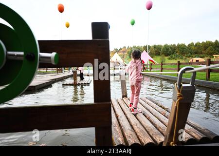 Kleines Mädchen, das auf einem hölzernen Pier in einem See beim Überqueren des Wassers spielt. Stockfoto