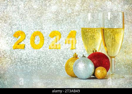 Frohes neues Jahr 2024. Zwei Gläser Champagner mit weihnachtskugeln und goldenen Zahlen mit der Zahl 2024 auf silbernem Bokeh. Silvester Stockfoto