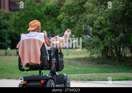 Älterer Mann, der mit den Beinen hoch im elektrischen Rollstuhl liegt und verschiedene Konzepte zeigt Stockfoto