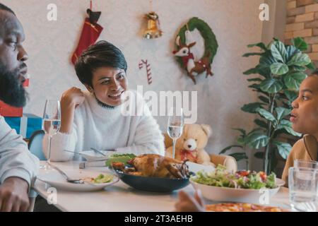 Porträt einer jungen Frau mit afroamerikanischem Ehemann, der das weihnachtsessen der türkei in einem dekorierten Zuhause mit Strümpfen, Zuckerrohr, Kranz, Geschenken und Glocken genießt Stockfoto