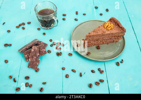 Kakaotortenscheibe mit Schokoladenstückchen und Kaffeebohnen auf einem blauen Holztisch Stockfoto