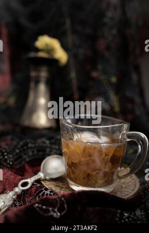 Kaffee oder schwarzer Tee mit Milch auf einem goldenen Tablett und einem silbernen Teelöffel, auf dunklem, unscharfem Hintergrund, selektiver Fokus in Nahaufnahme Stockfoto